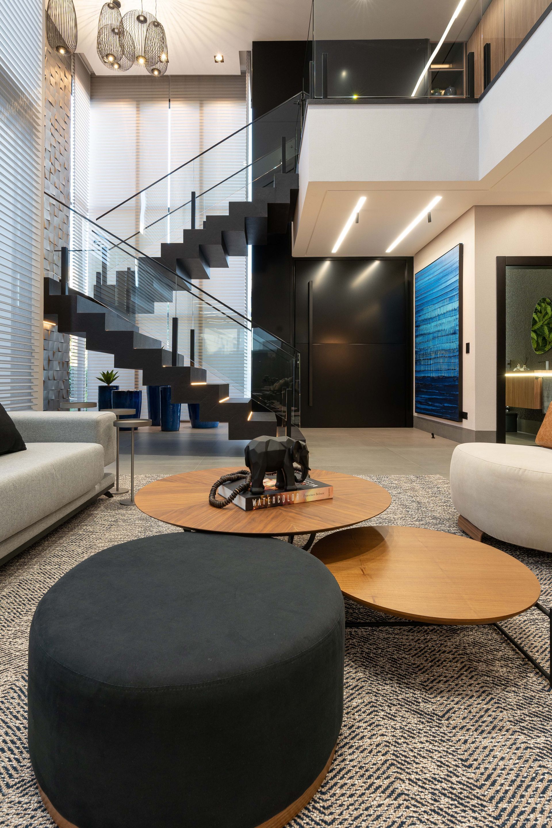 Sala de estar moderna com escada flutuante, parede preta e mesas de centro redondas.