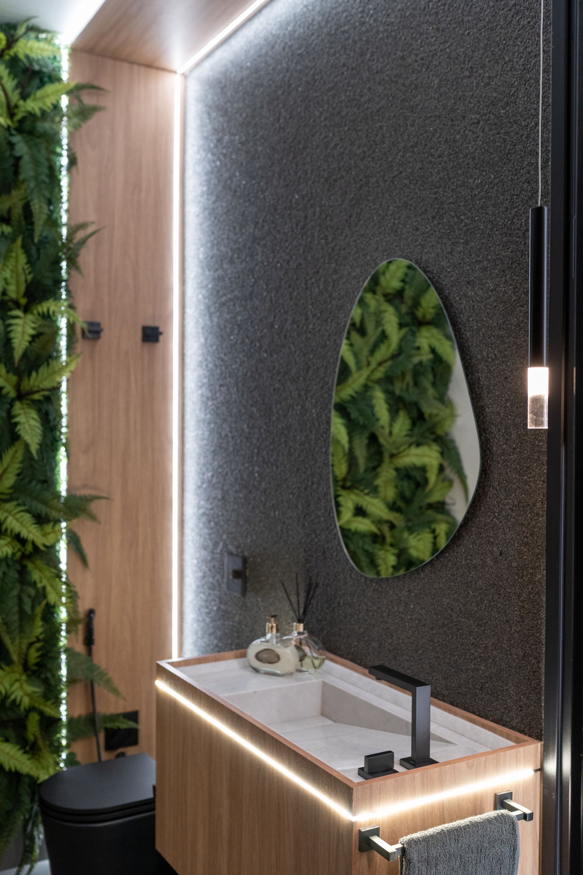 Banheiro moderno com parede verde, parede com detalhes em pedra, penteadeira de madeira e espelho em formato orgânico.