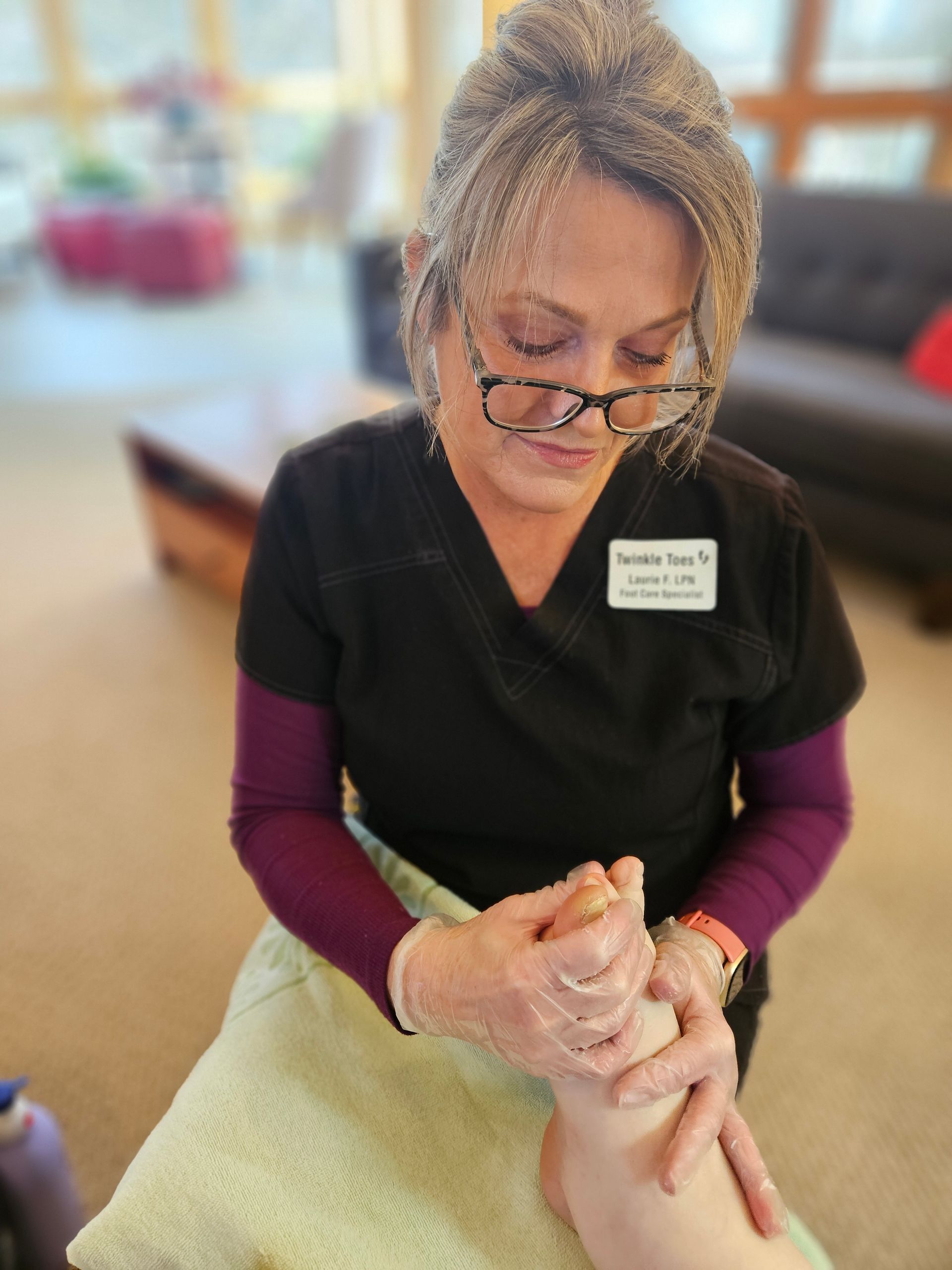 Nurse Laurie wearing gloves, performs a foot massage in a room with a couch and blurred background.