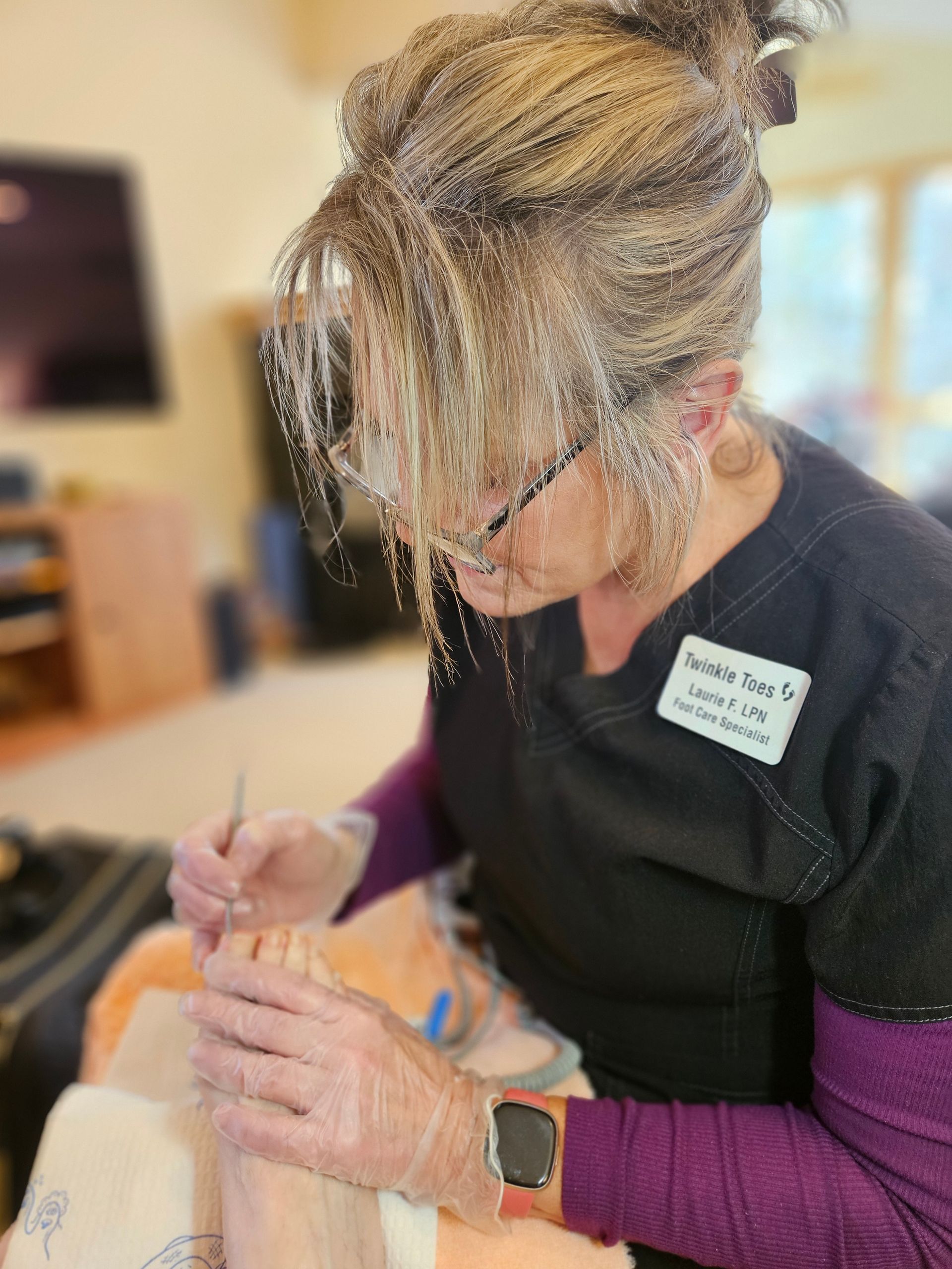 A professional in scrubs wears gloves and uses a tool to perform a foot care.