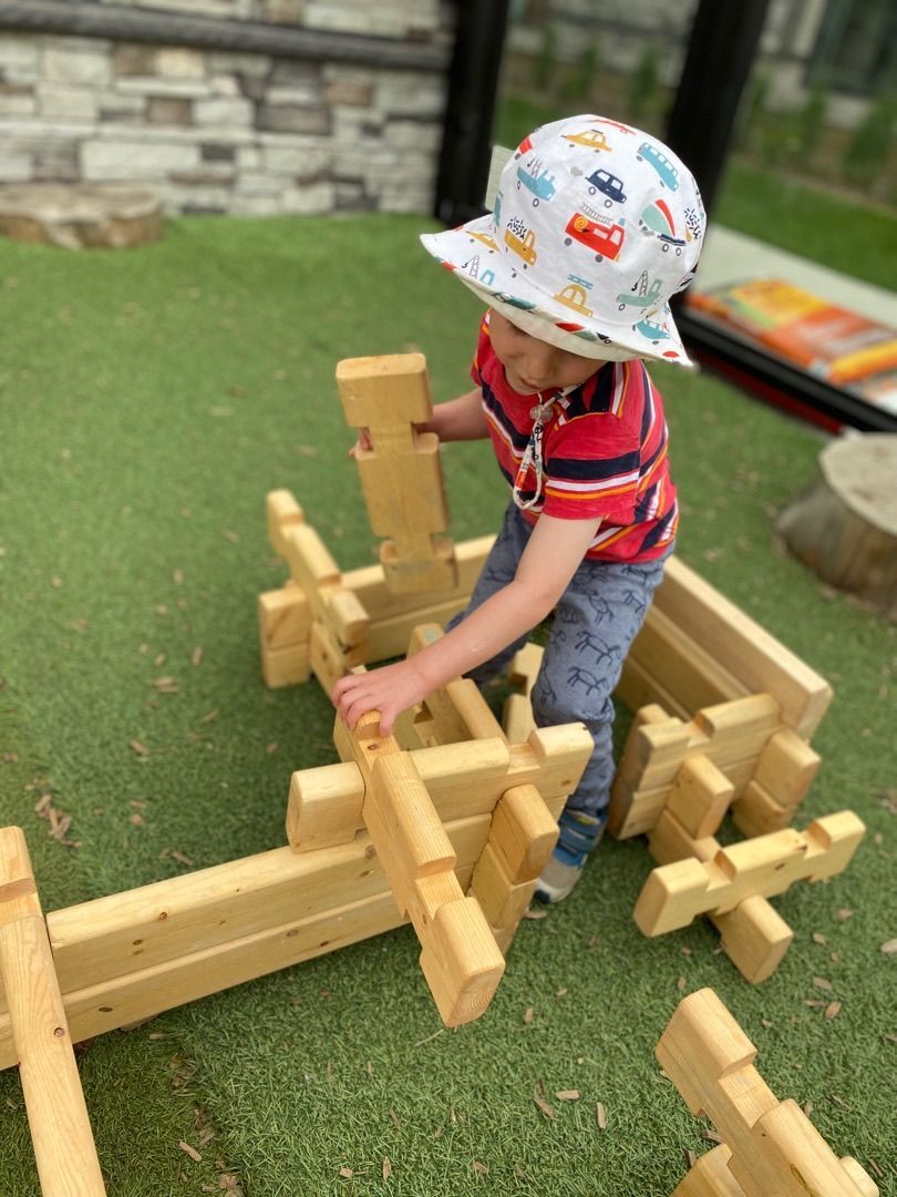 Child in a white helmet stacking wooden blocks on grass outdoors