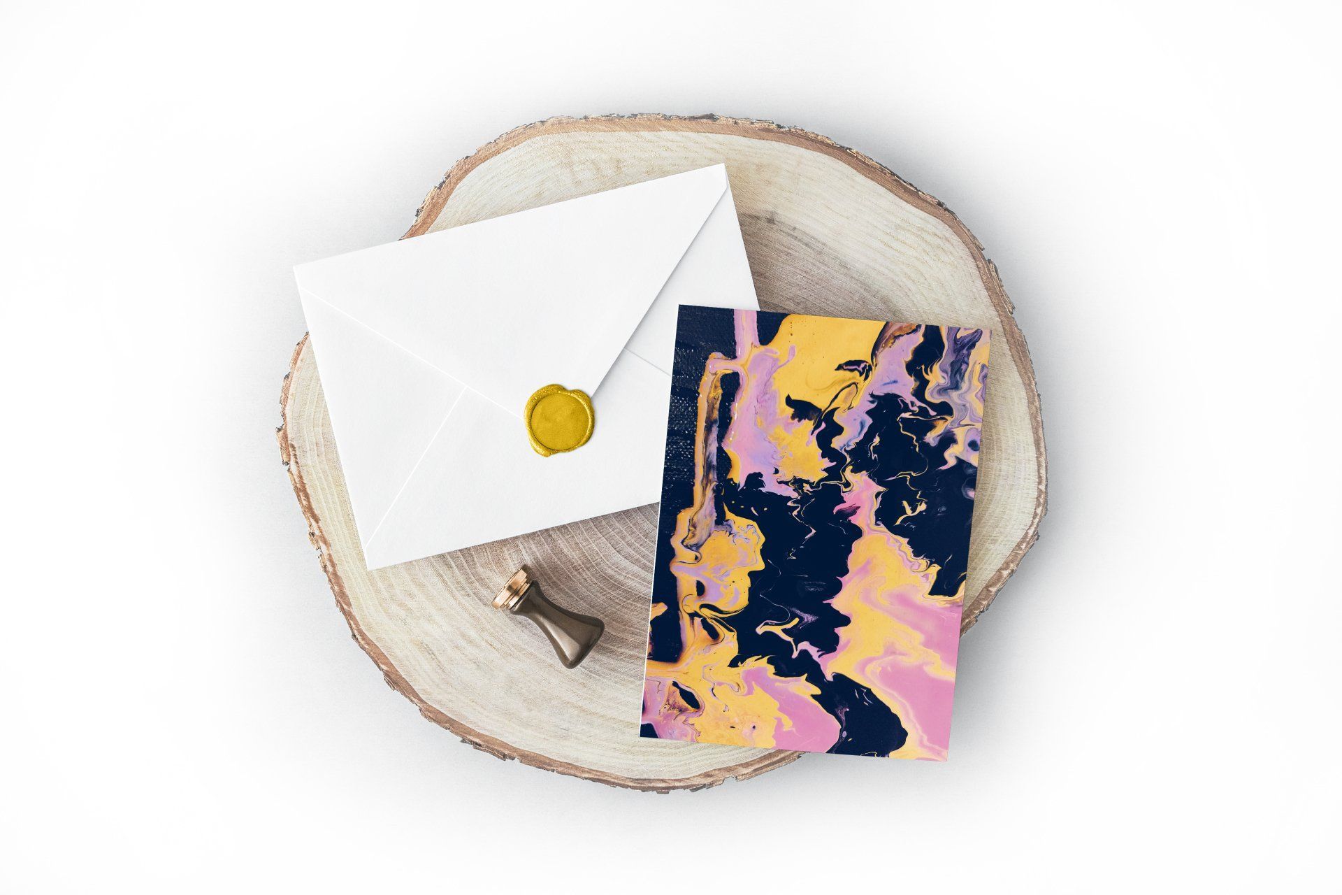 White envelope with gold seal, marbled notebook, and stamp on a wood slice.