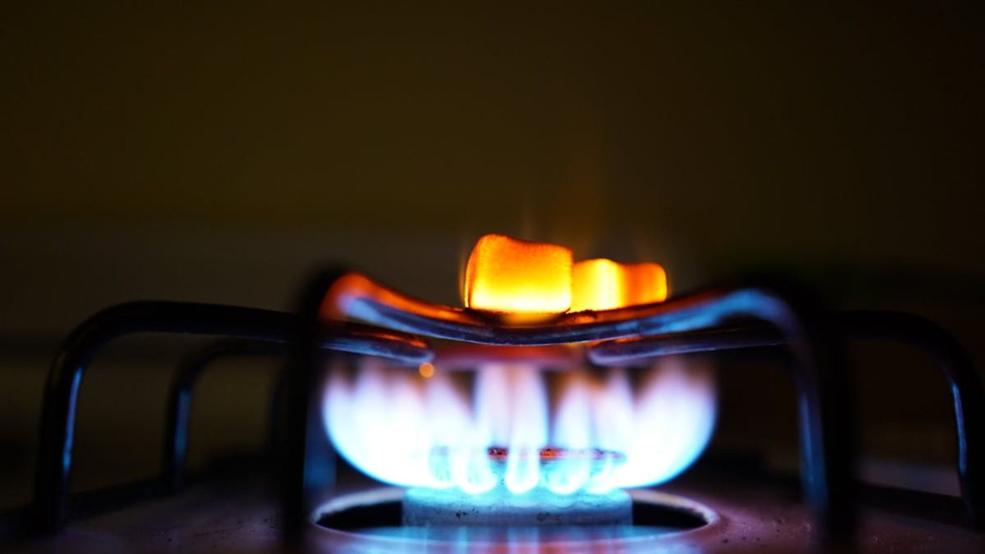 El quemador de la estufa de gas se enciende y las llamas brillan en azul y naranja.