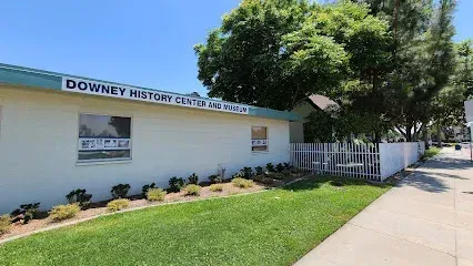 Tree Services West Covina-One-story building of Downey History Center and Museum, with a white exterior, blue trim, and small landscaped garden; bright, sunny day with clear sky.