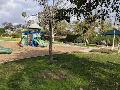 Tree Services West Covina-A sunny playground with multiple blue and yellow slides, climbing structures, and ladders on a rubber floor, surrounded by trees and clear skies.