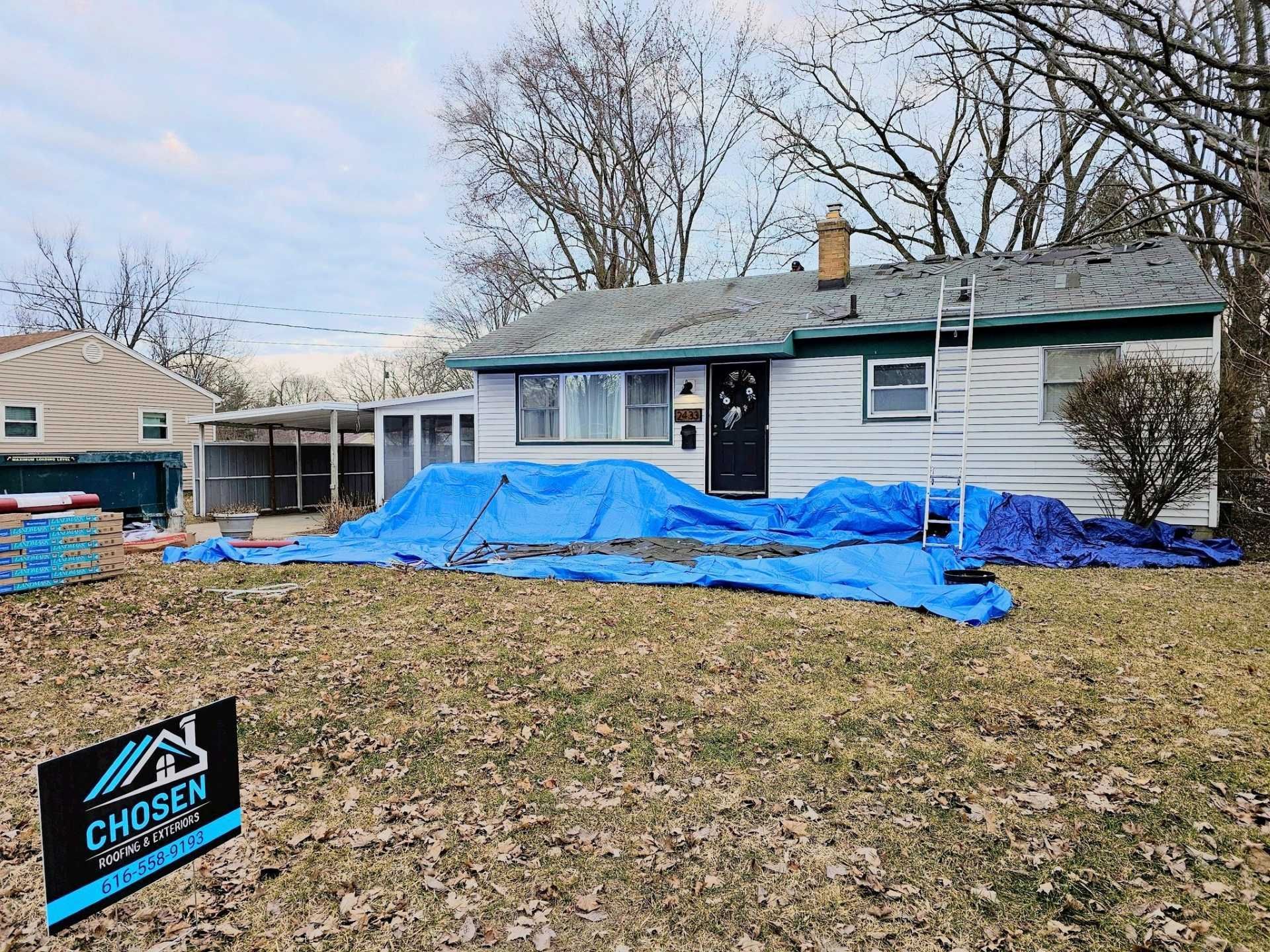 A house under renovation with blue tarps covering the front yard and a Chosen Roofing sign in the foreground.