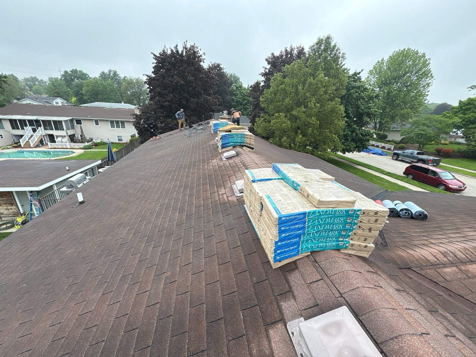 Workers on a brown shingled roof with stacks of new roofing materials during a residential roof replacement.