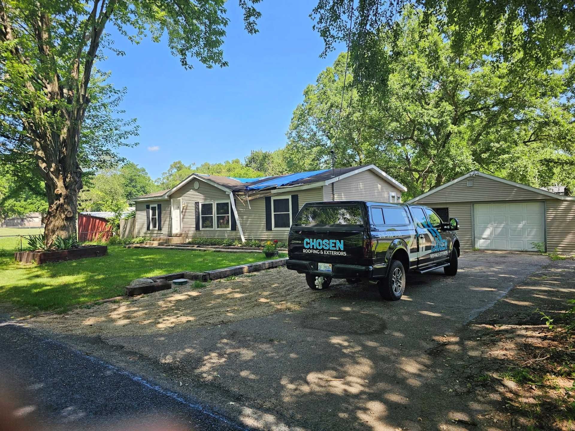 A light-colored, single-story suburban home with a gravel driveway, a black truck parked in front, and a detached garage.