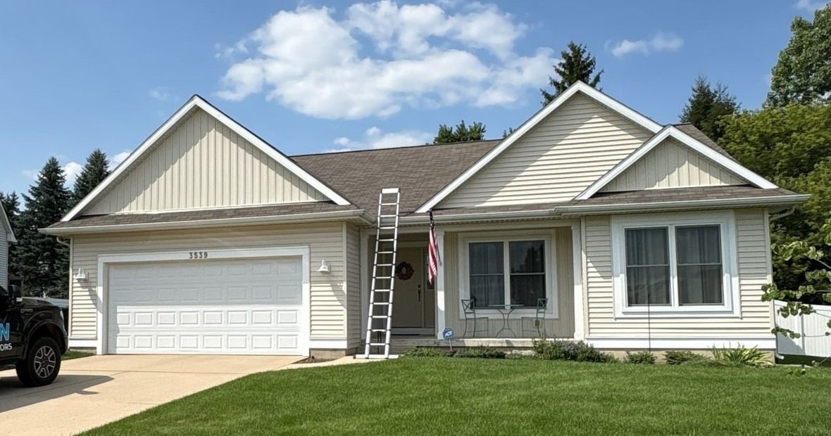 A light-colored, single-story suburban house with a two-car garage and a ladder leaning against the roof.