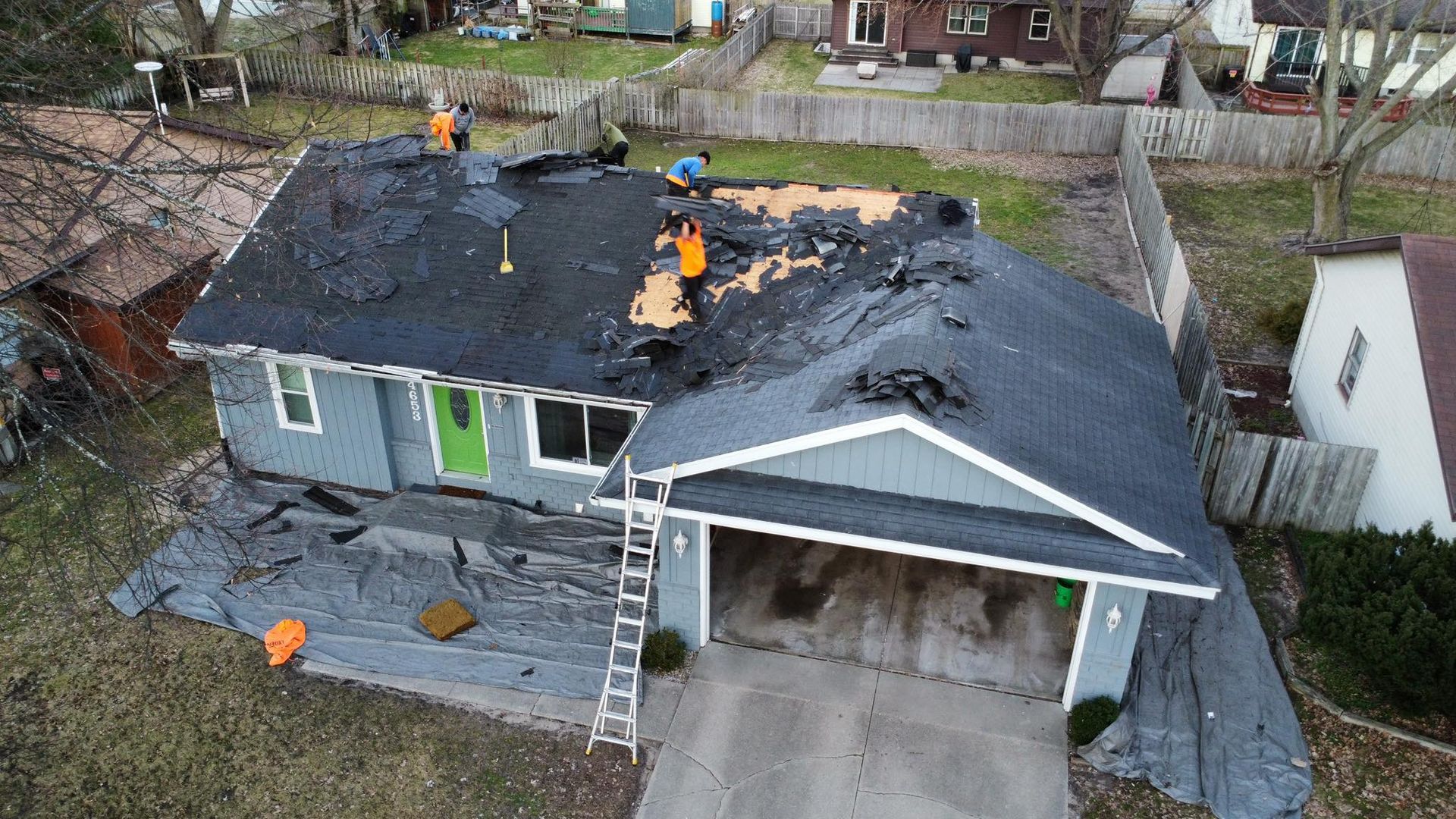 Aerial view of a residential house with a partial roof replacement in progress, featuring workers on the roof.