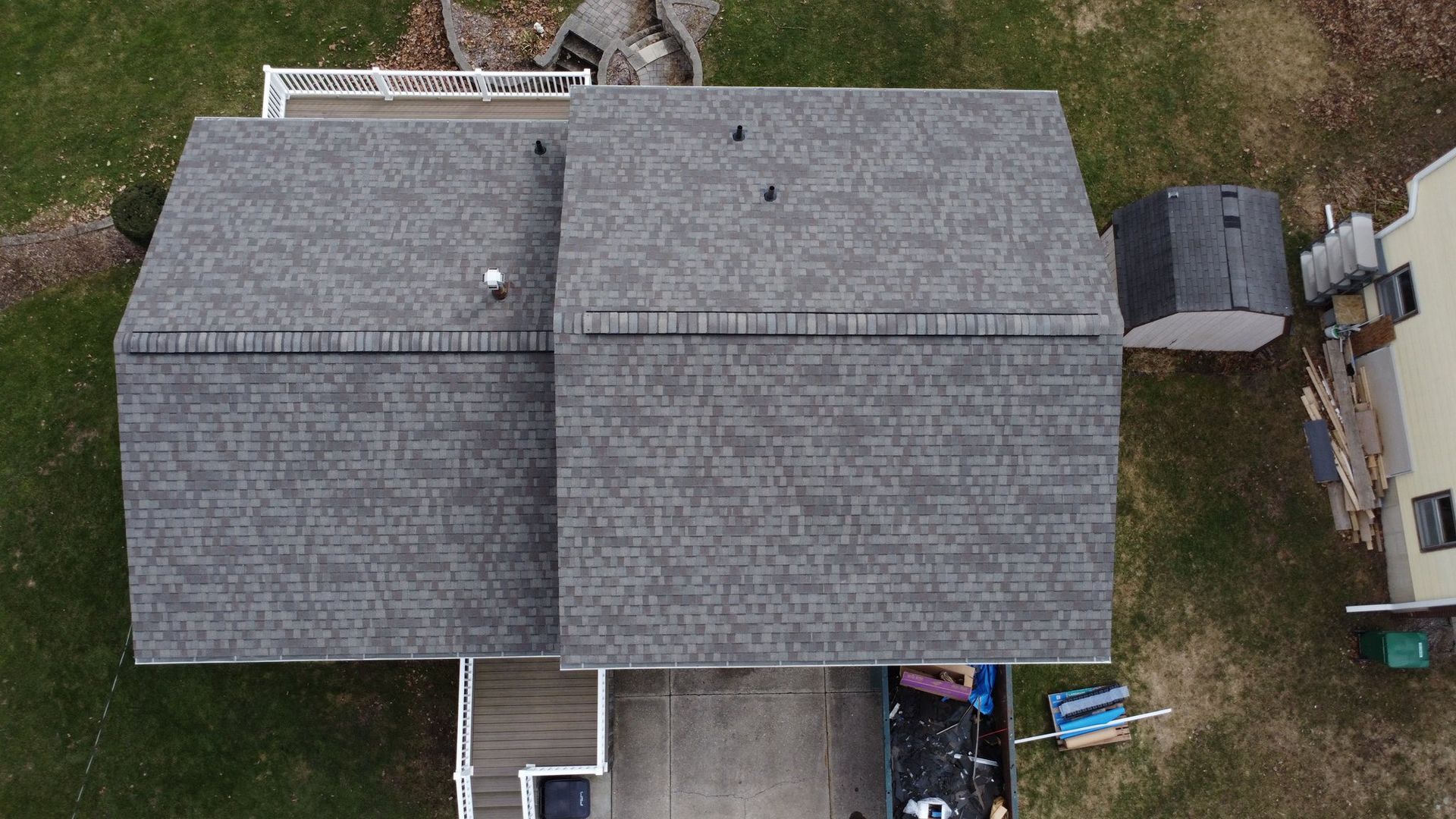 An overhead aerial view of a house roof featuring gray shingles, a chimney, and adjacent lawn and driveway areas.