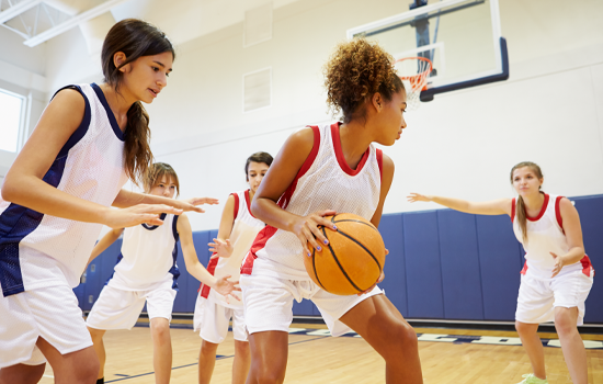 Girls playing basketball in a gym, dribbling and defending during practice.