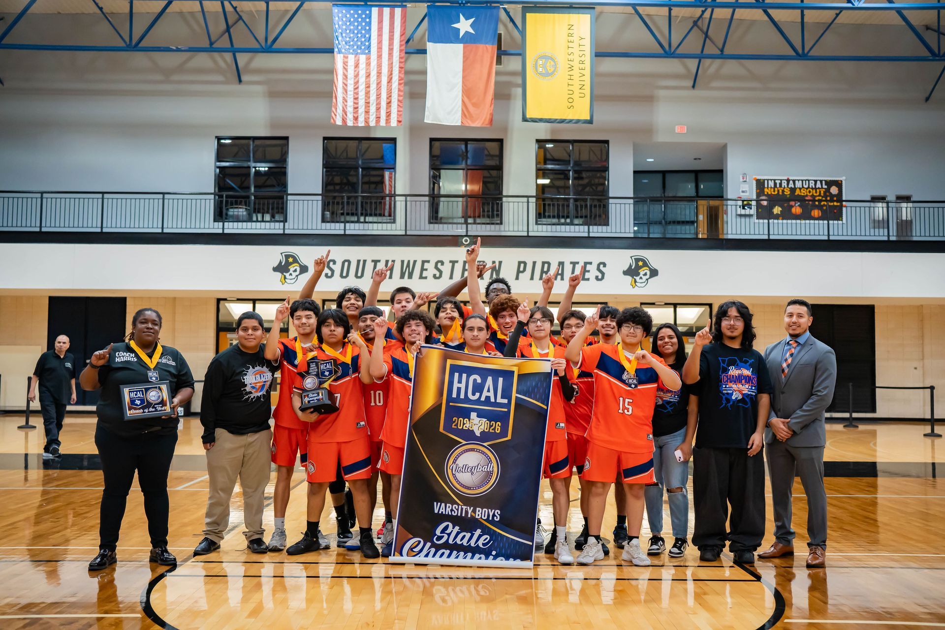 Youth basketball team and coaches posing on a gym court with a championship banner and basketballs.