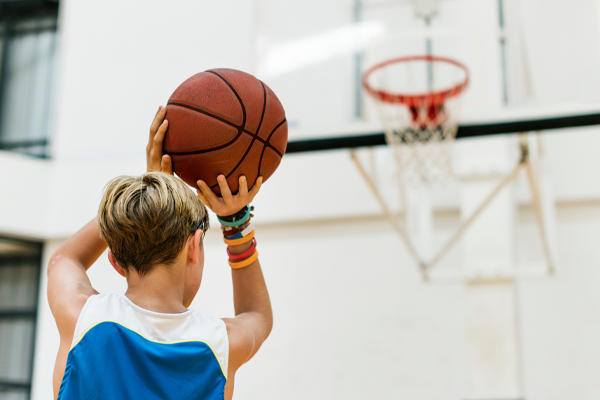 Child in a blue jersey shooting a basketball toward an indoor hoop