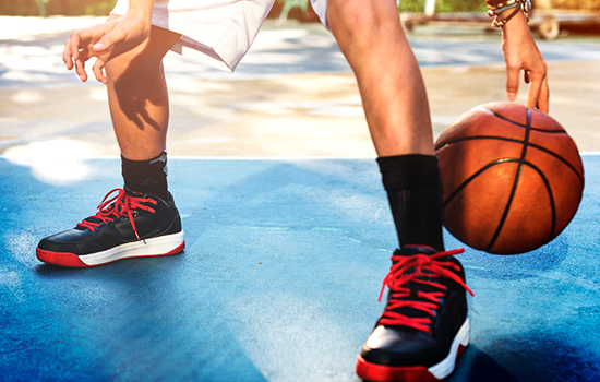Basketball player dribbling on a blue outdoor court, wearing black and red sneakers