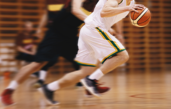 Basketball player in white dribbling fast past a defender on a court