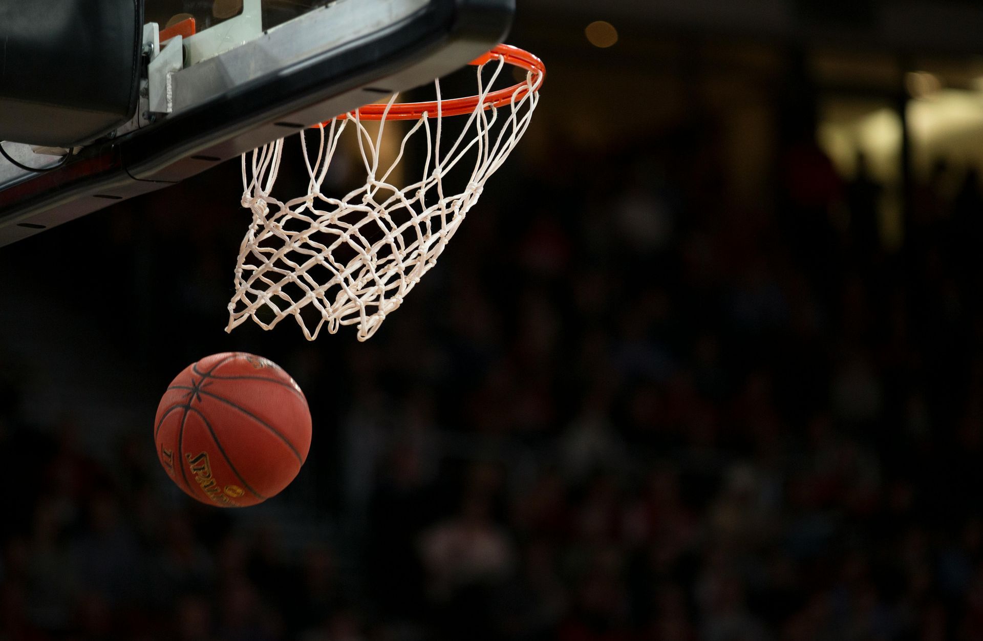 Basketball falling toward the hoop with a white net on a dark court background