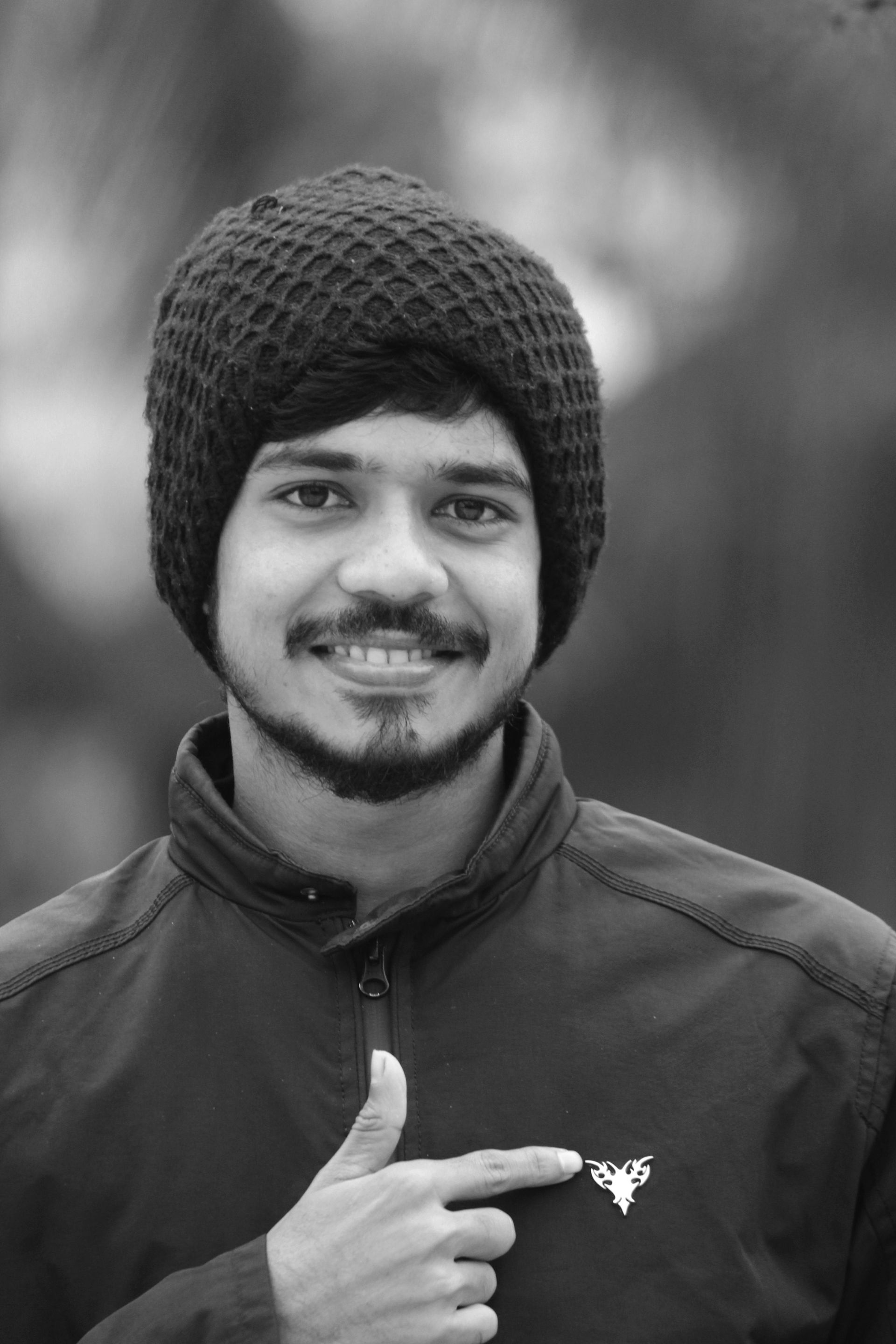 Smiling person in a knit beanie and jacket points at a small logo on the chest.