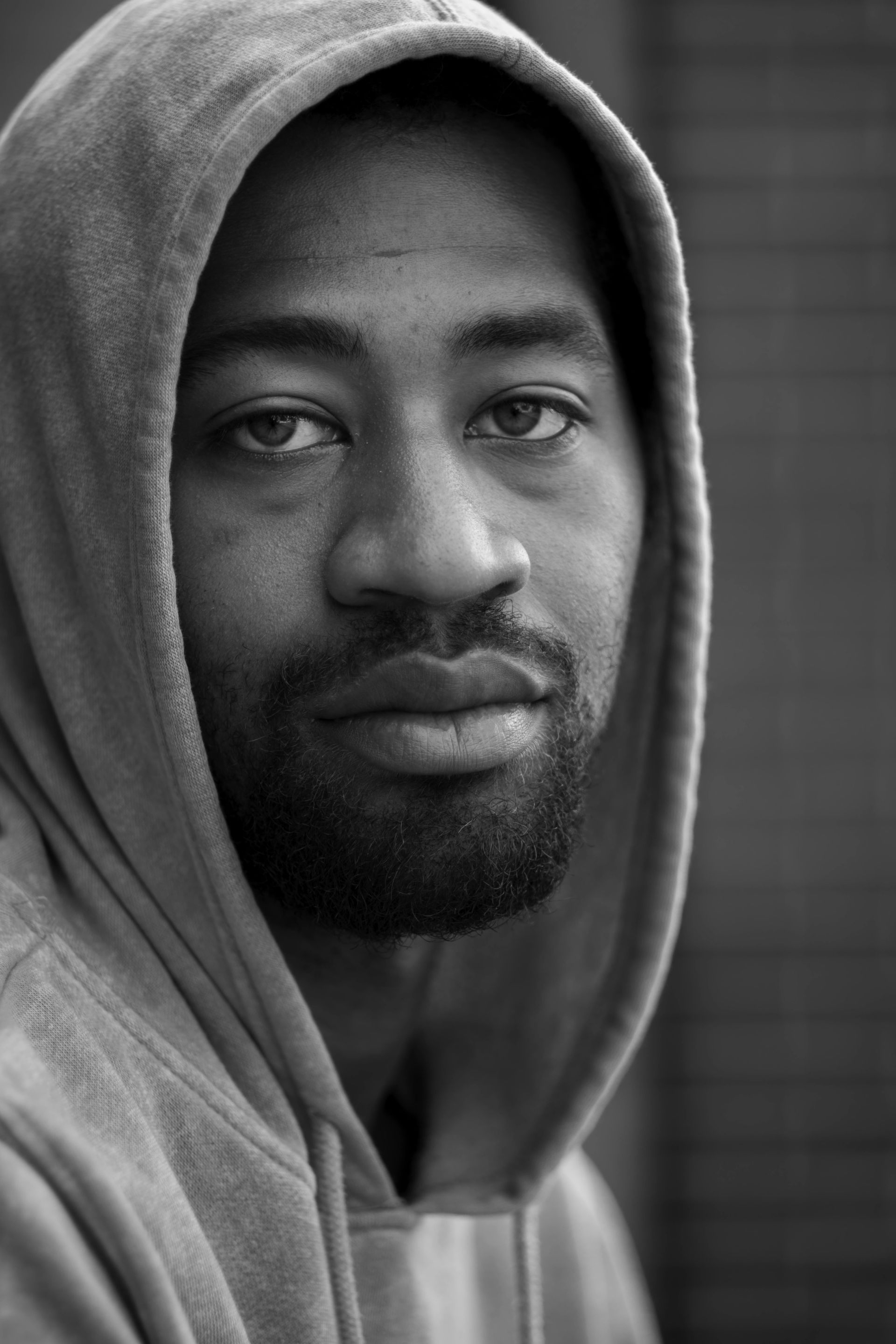 Portrait of a man in a hoodie, looking at the camera against a blurred background.