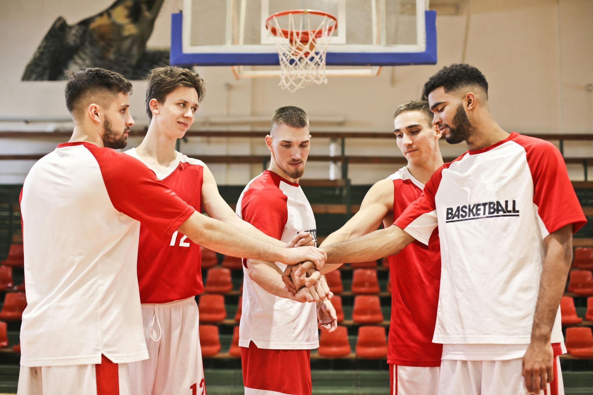 Basketball team in red and white uniforms huddling with hands together on a court