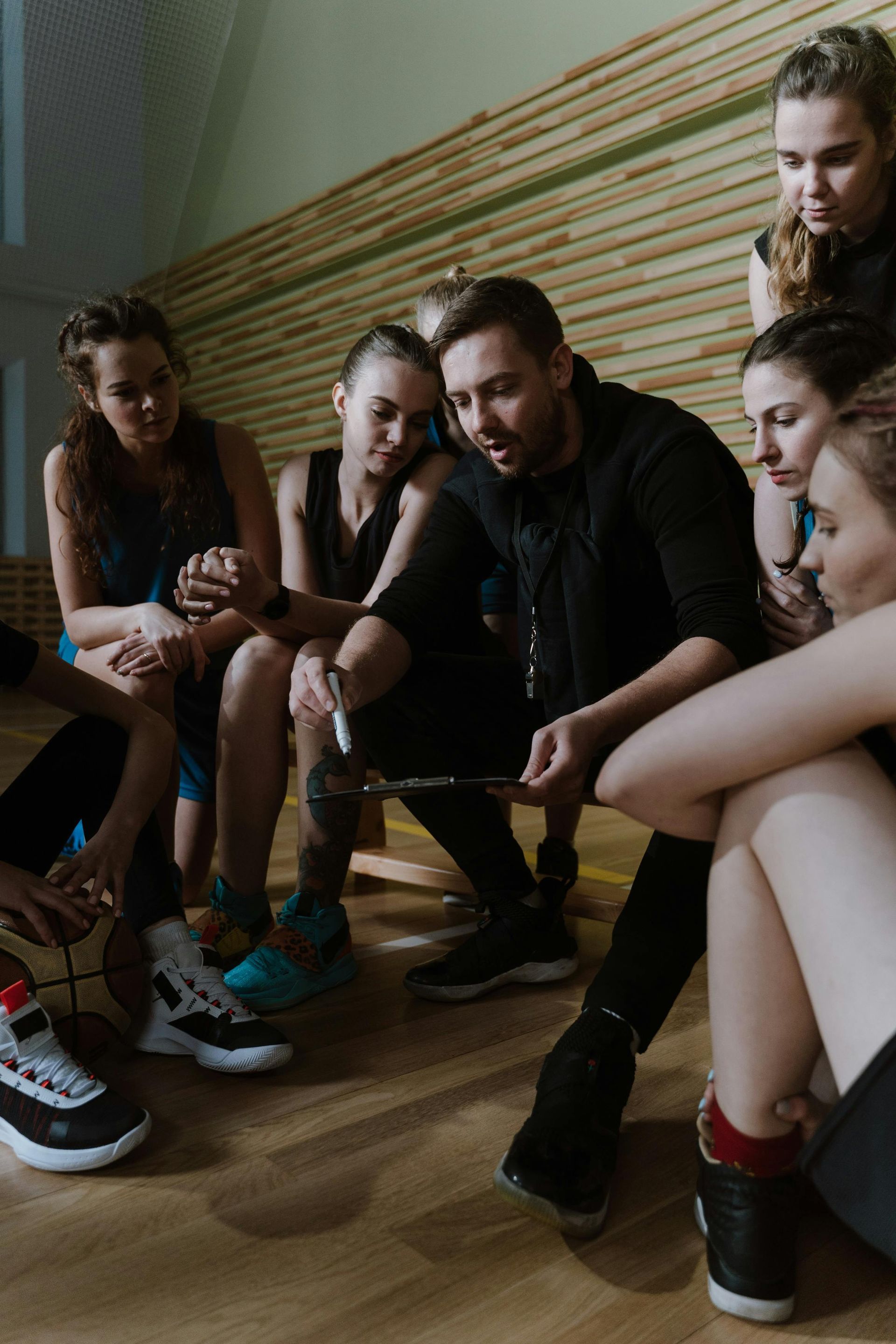 Group seated on a wooden floor, leaning in and listening together in a small room.