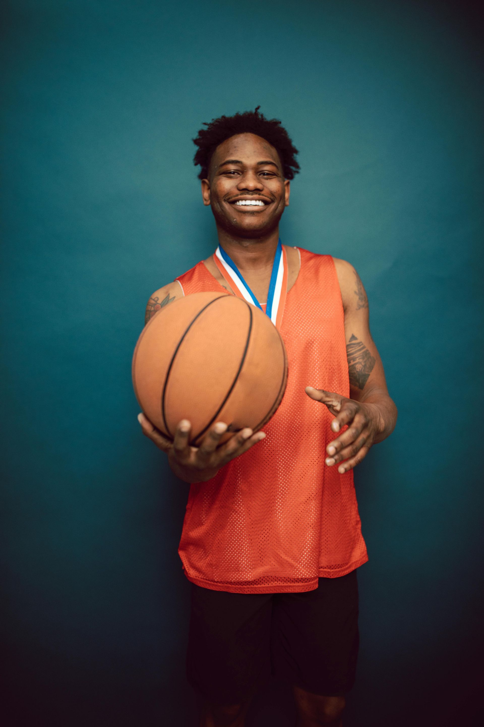 Smiling basketball player in orange jersey holding a ball against a teal background