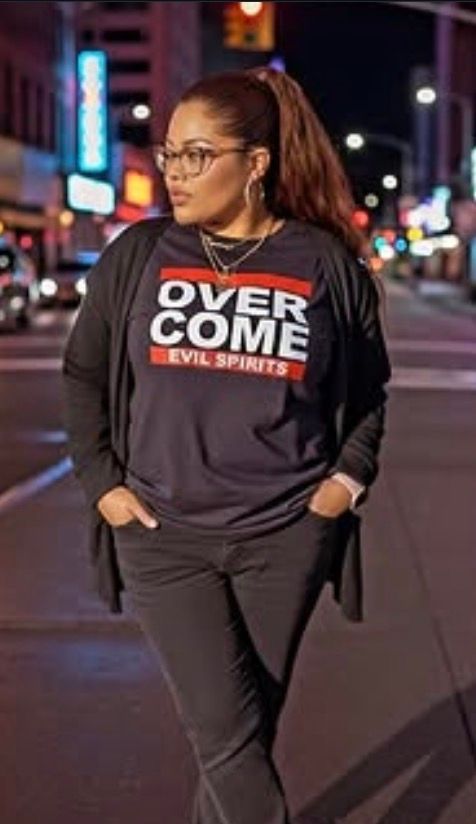 Woman in black “OVERCOME EVIL SPIRITS” outfit standing on a city street at night.