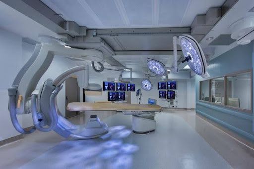 Uma sala de cirurgia moderna e bem iluminada com equipamento cirúrgico, monitores e uma mesa para pacientes.