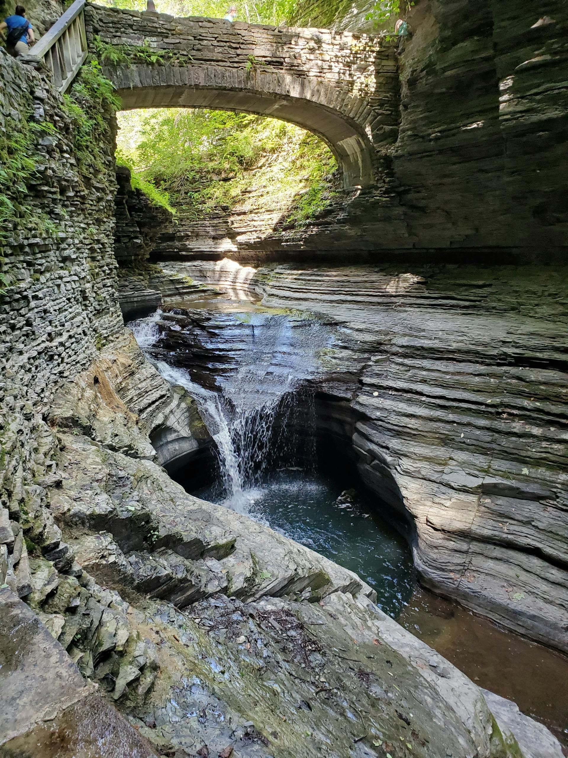 A waterfall in a canyon with a bridge over it.