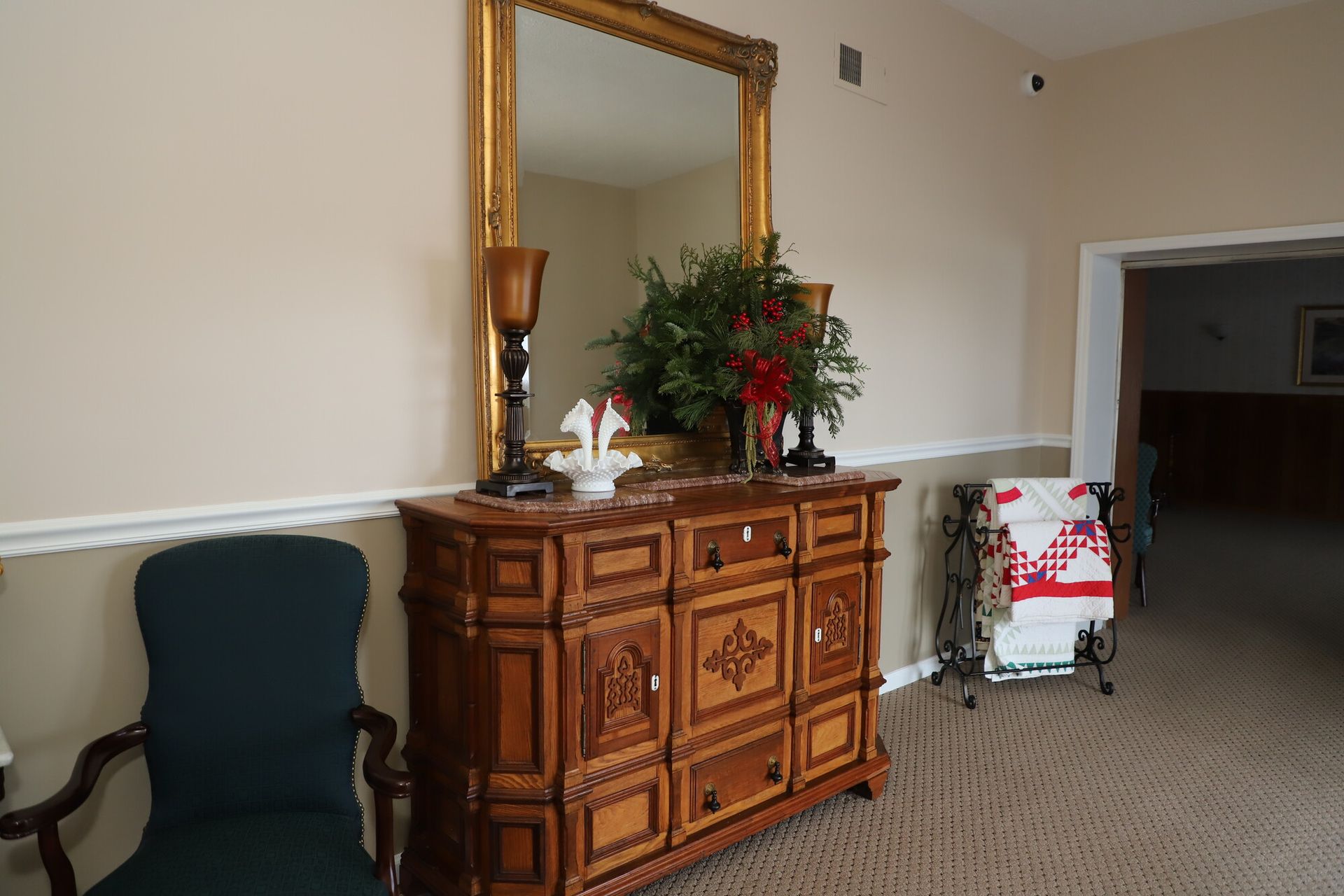 Decorative cabinet with large mirror and flowers in a beige room, with a chair and shopping cart nearby