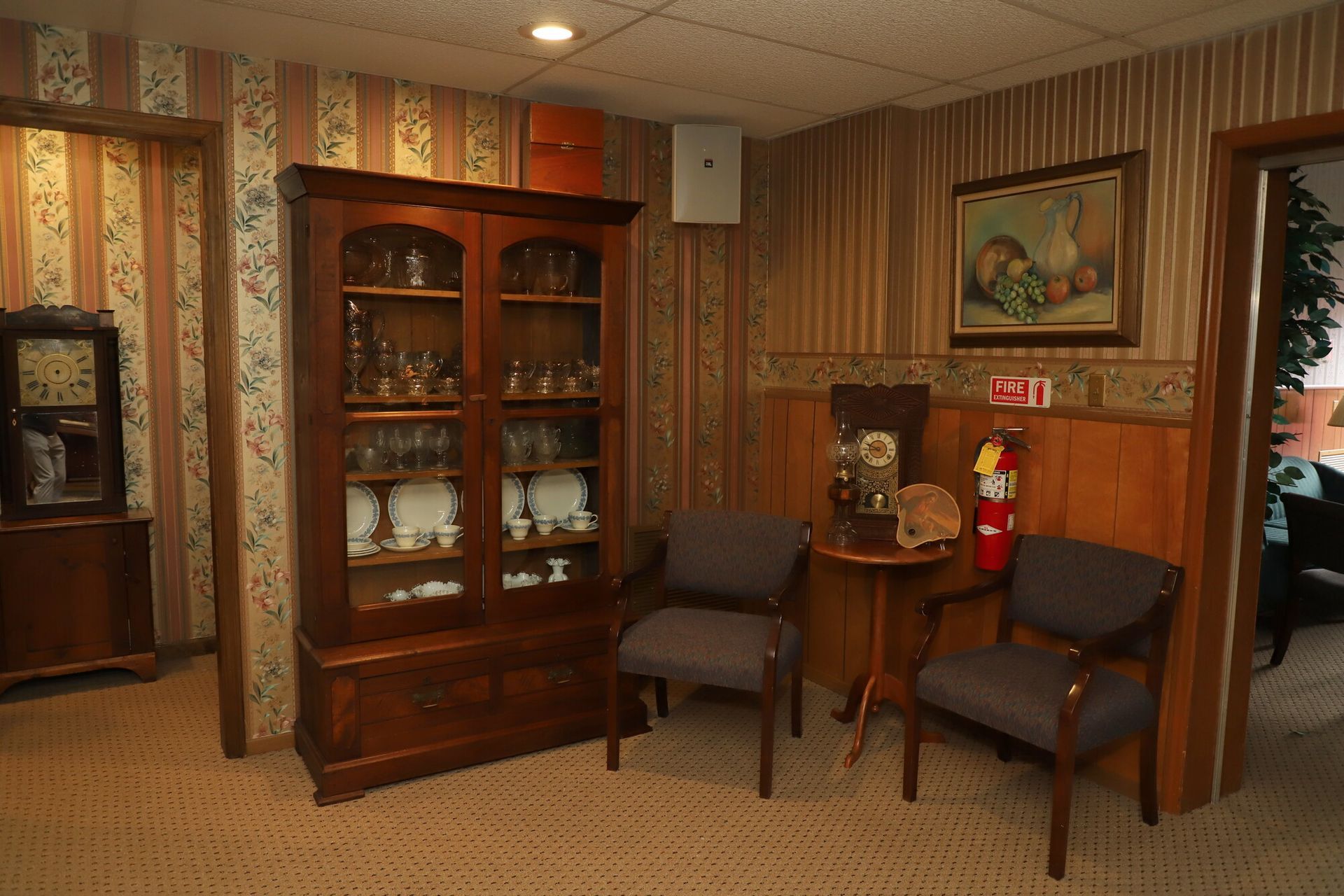 Wood-paneled room with china cabinet, chairs, small table, and framed wall art
