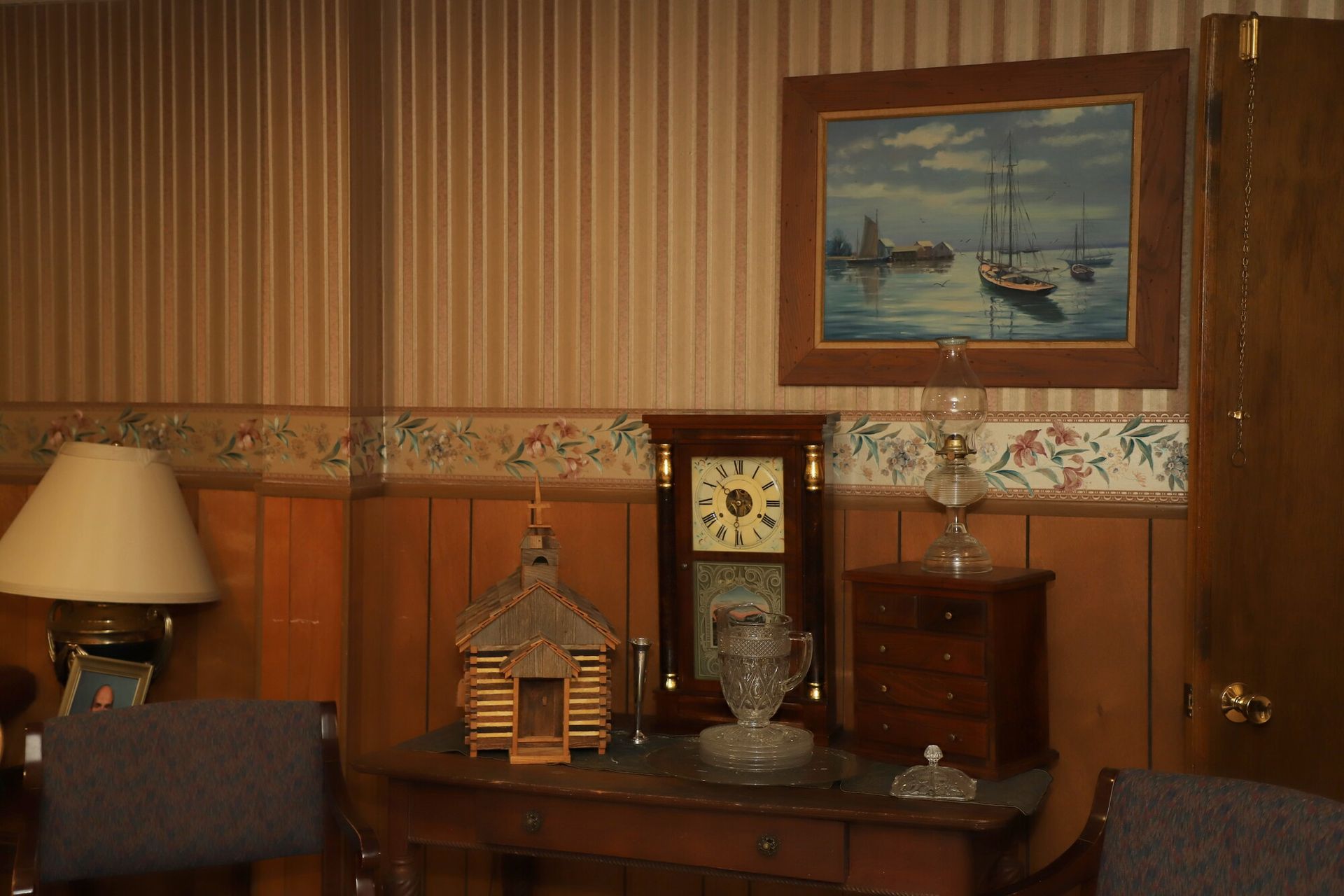 Warm living room with wood paneling, striped wallpaper, lamp, sideboard, and framed seaside painting