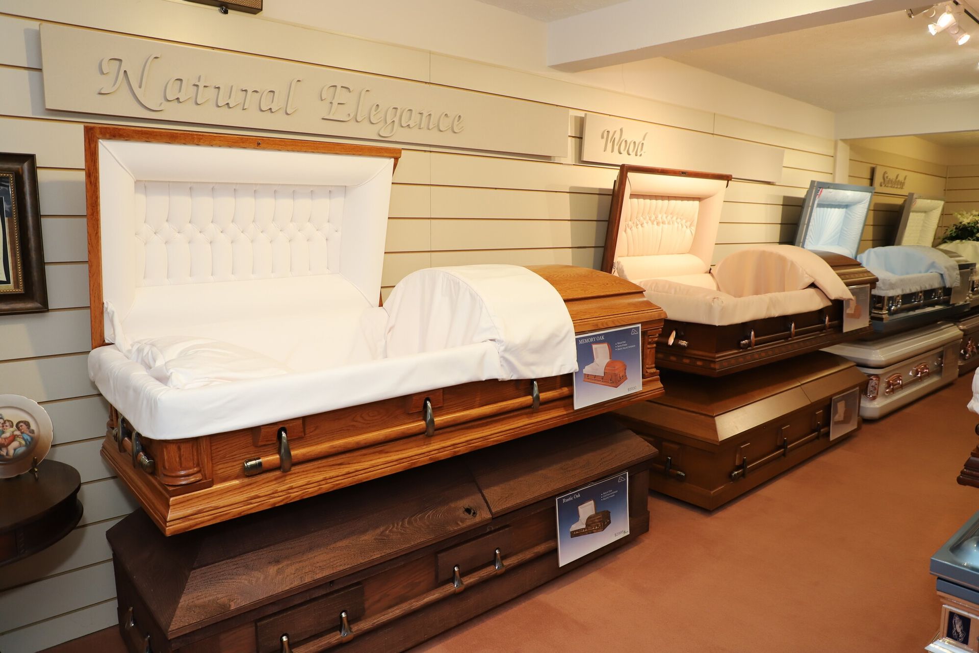 Three ornate caskets on display in a funeral showroom with carved wood and white interiors