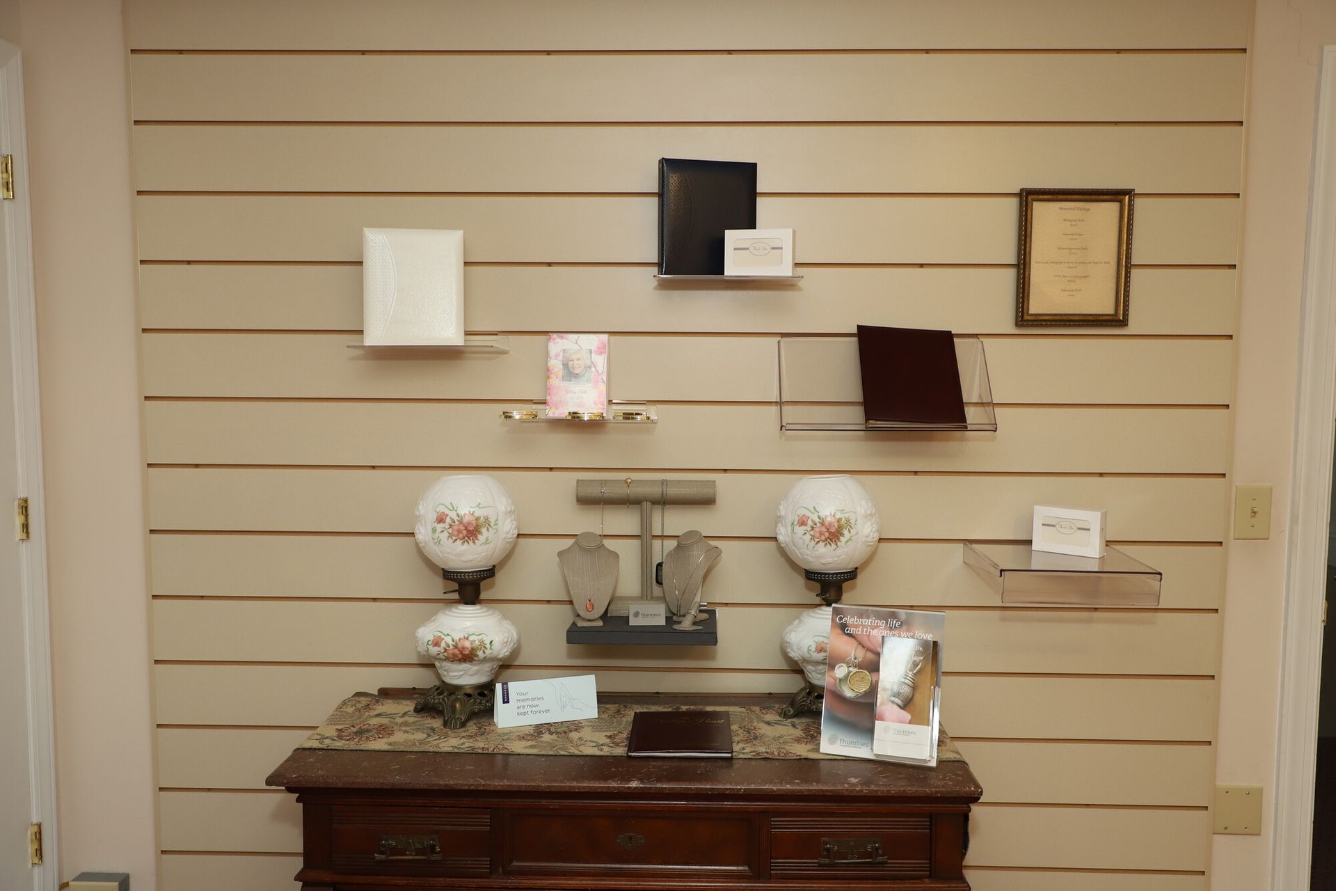 Display of decorative dishware and framed items on a slat wall above a wooden table