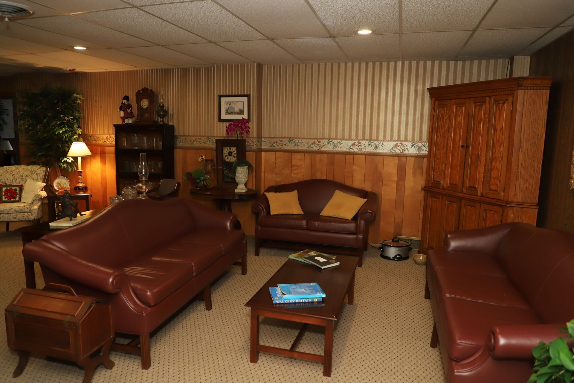 Cozy living room with brown leather sofas, coffee table, lamp, and wooden cabinet against striped walls