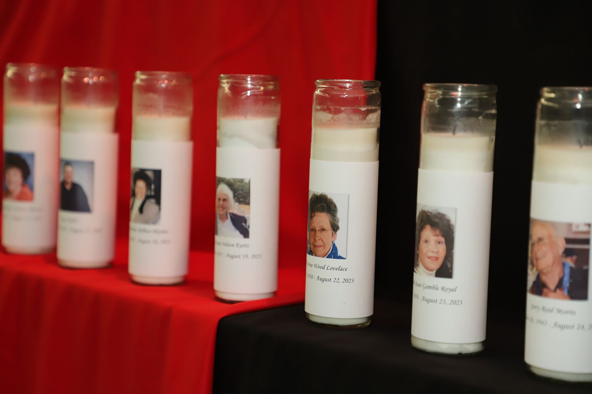 Lit candles with photos of people displayed on a red tablecloth, suggesting a memorial tribute