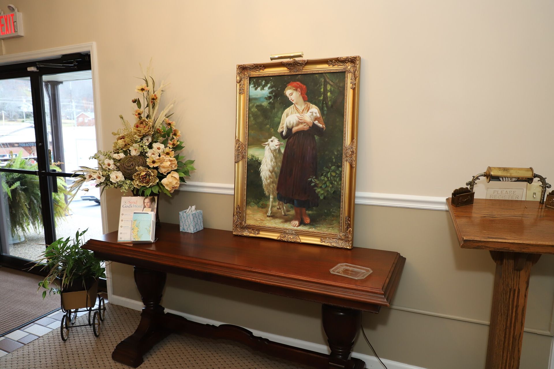Lobby table with a framed portrait, floral arrangement, and candle stands against a beige wall