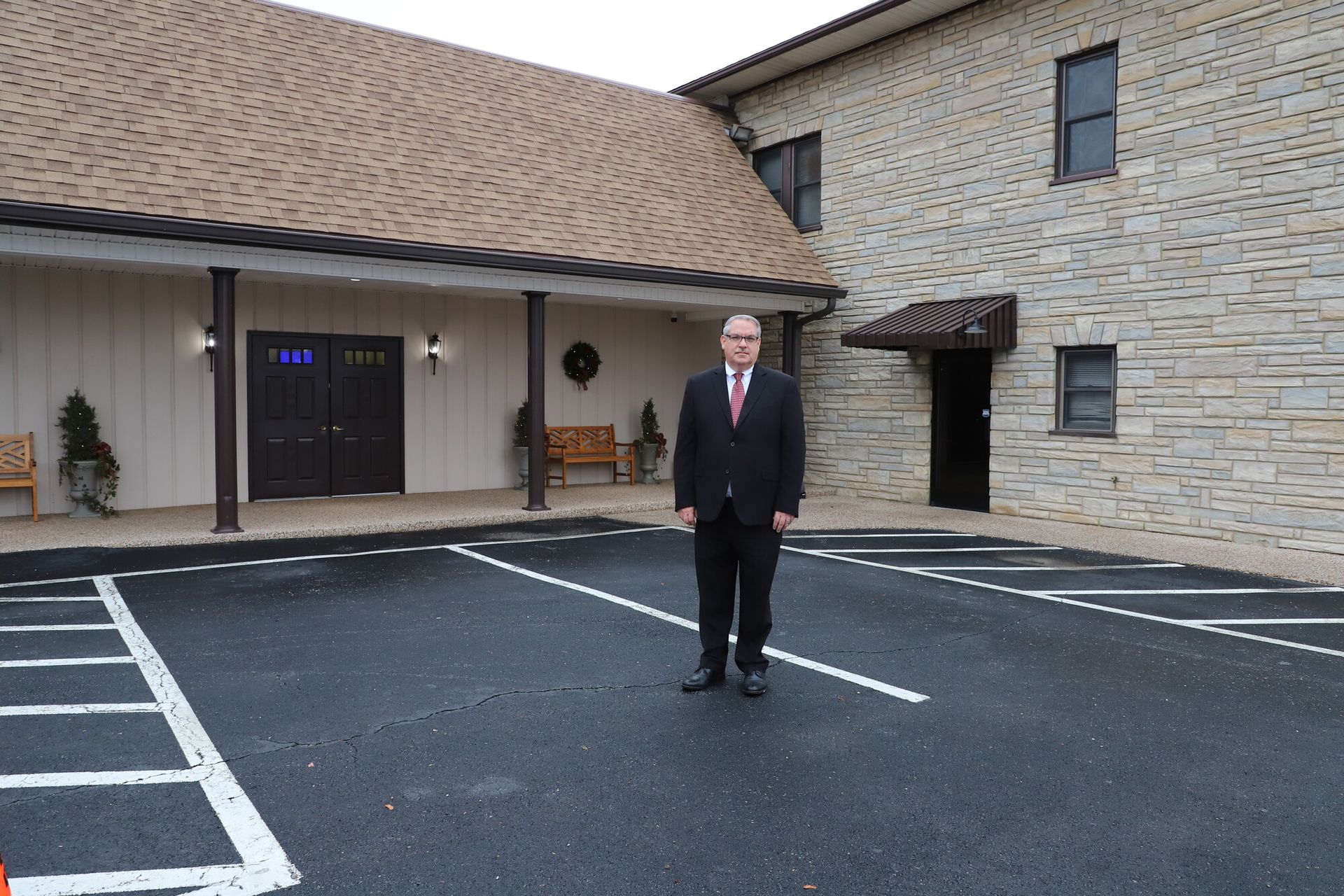 Man in a dark suit standing in a parking lot outside a brick building entrance