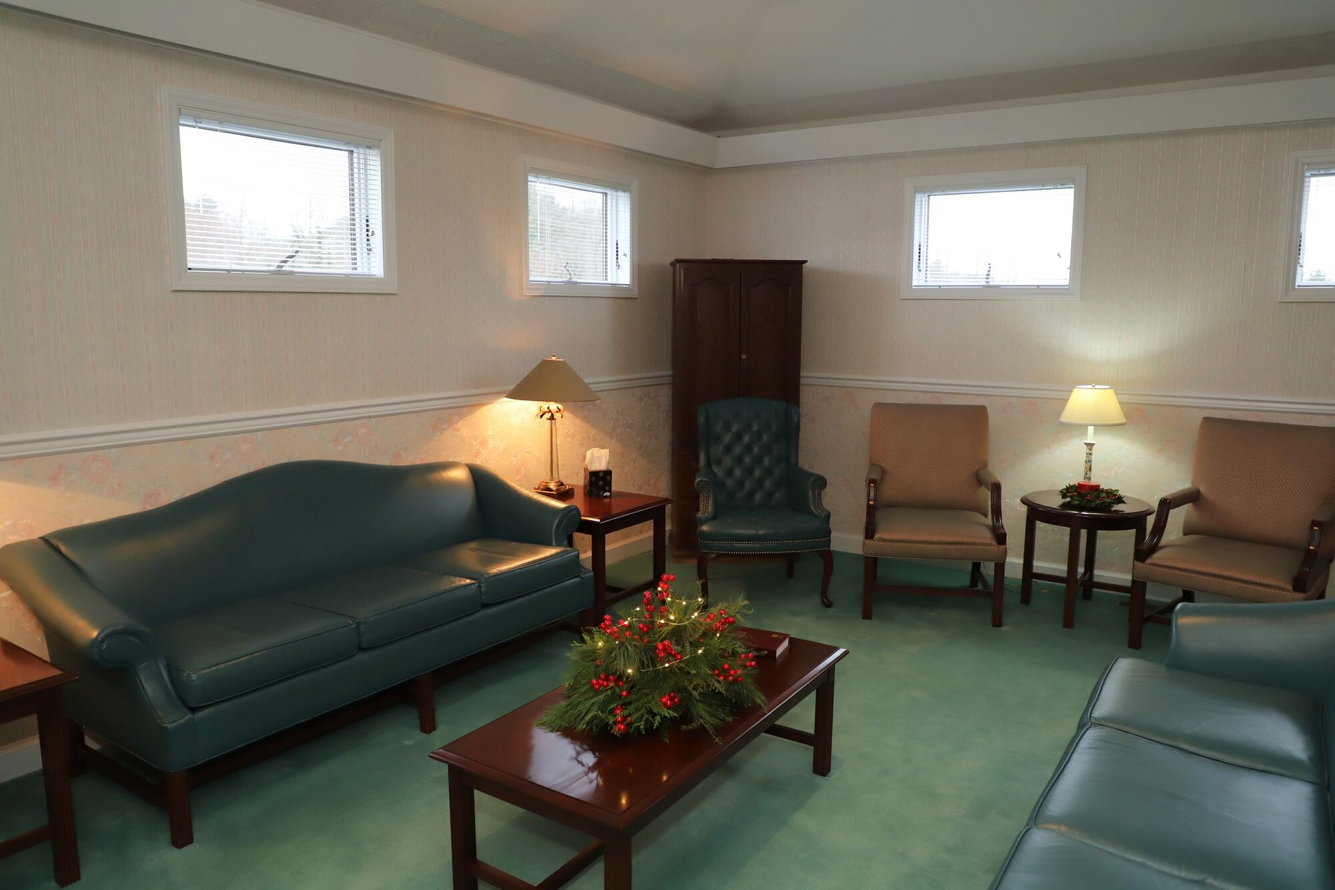 Cozy living room with green sofas, armchairs, coffee table, lamps, and high windows.