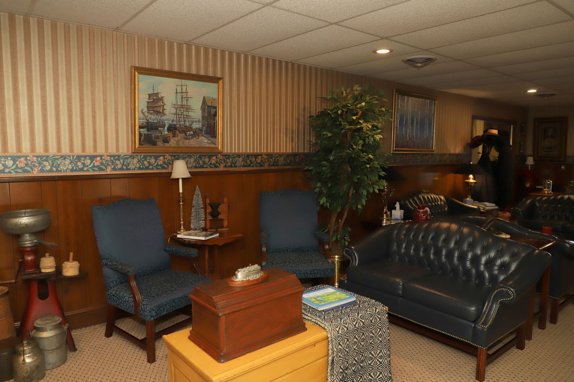 Cozy lounge with blue chairs, black leather sofa, wooden tables, and warm striped wallpaper.