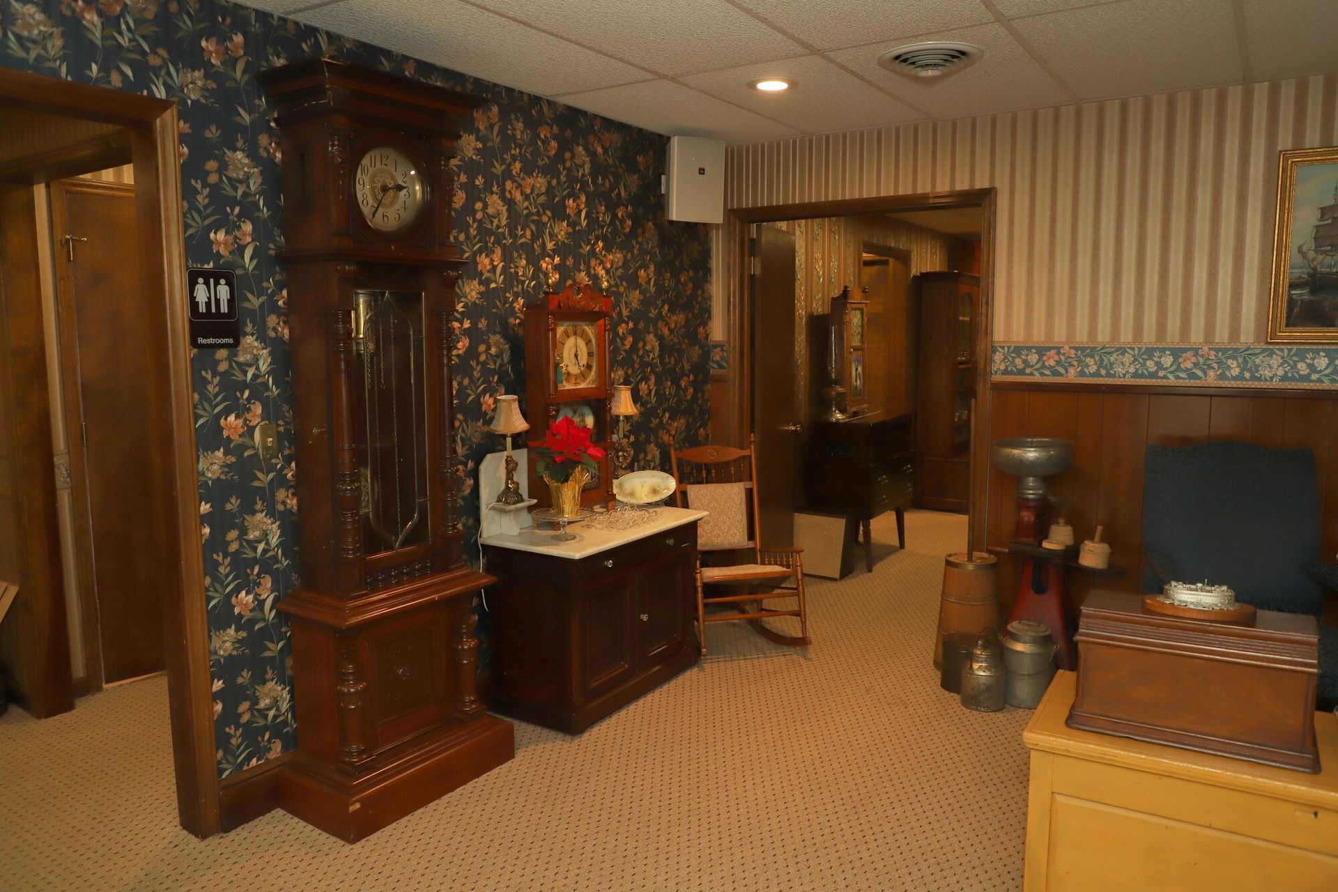 Cozy living room with fireplace, grandfather clock, patterned wallpaper, and wooden furniture