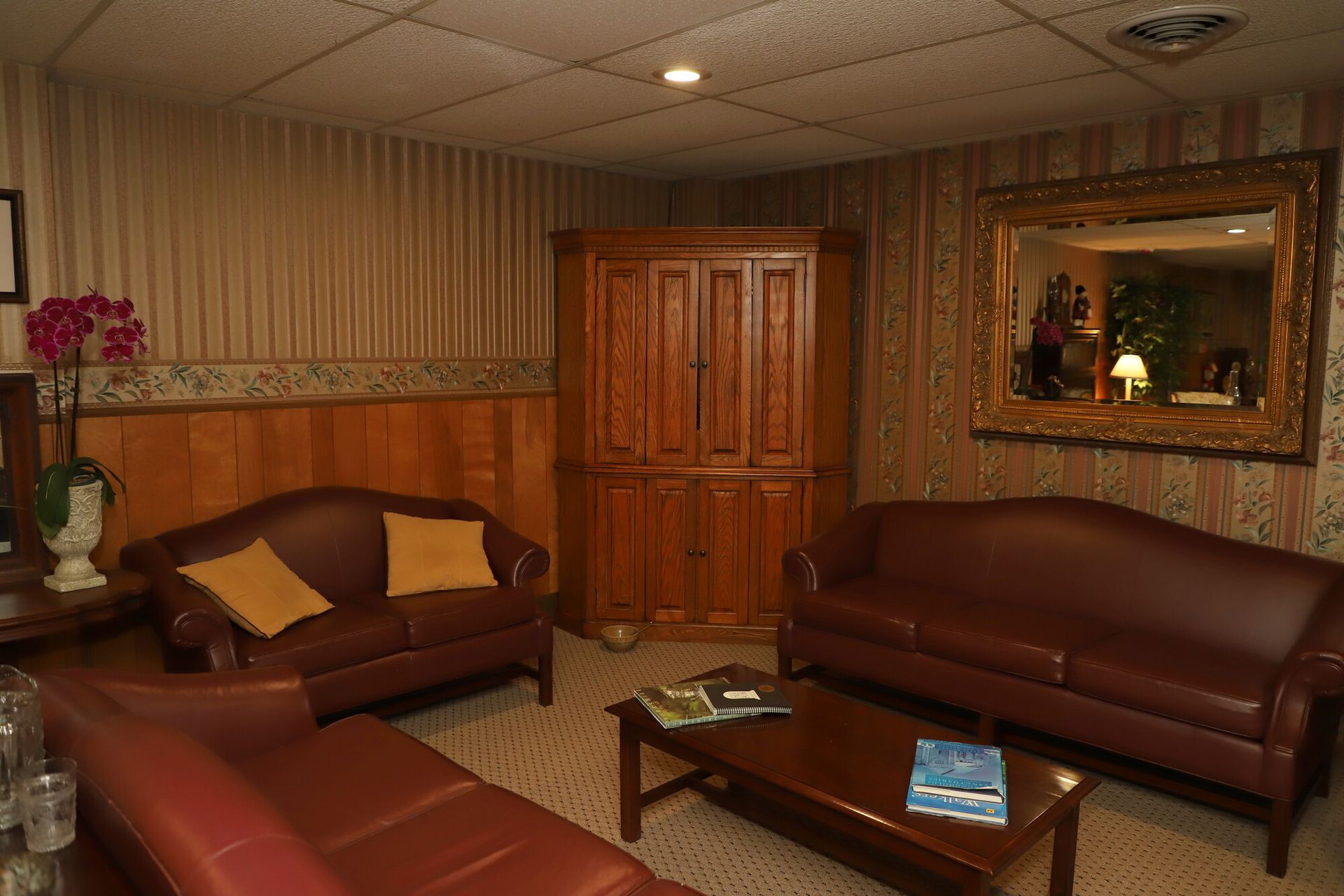 A cozy living room with brown leather sofas, a wooden cabinet, coffee table, and framed wall mirror.