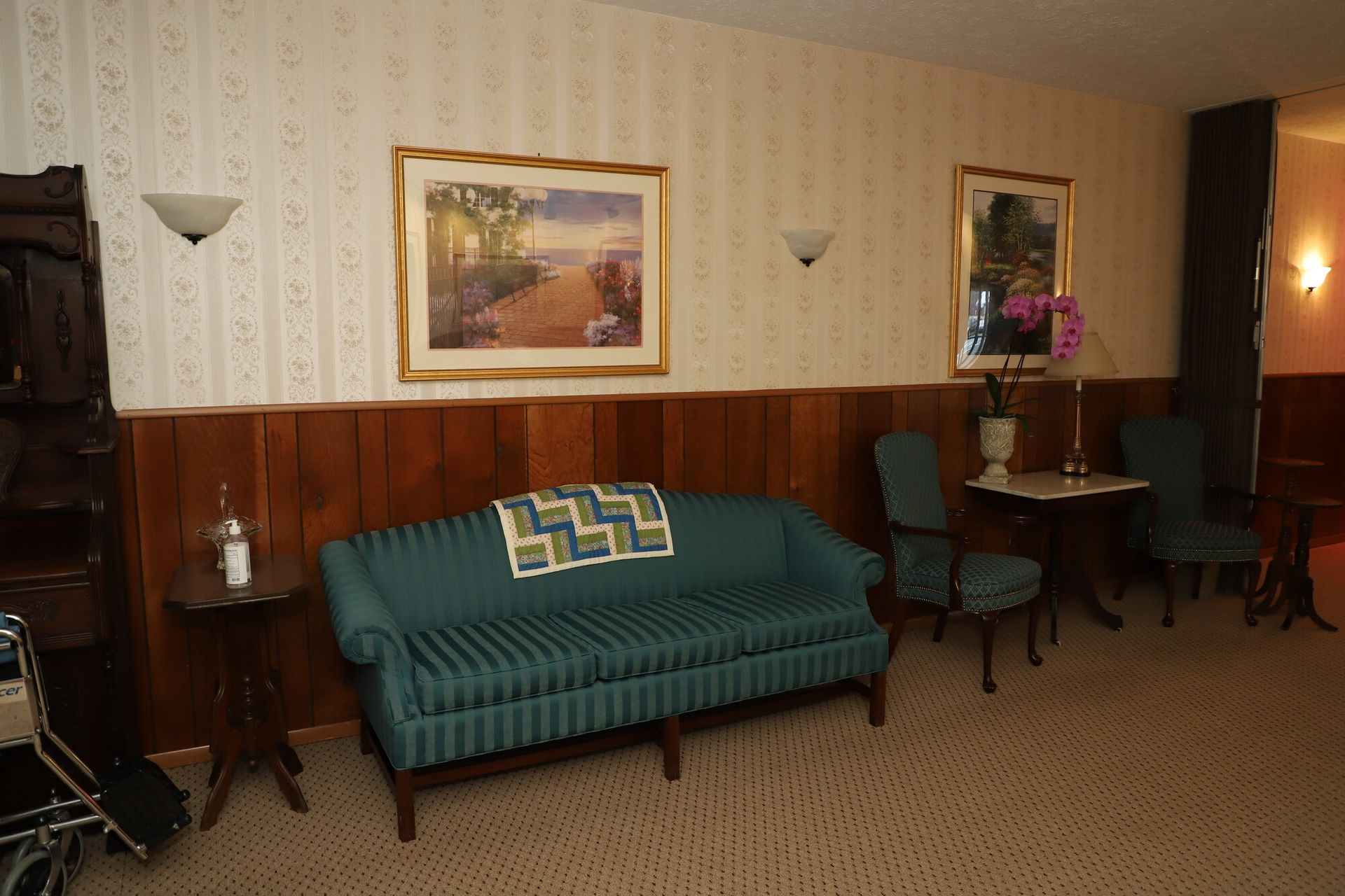 Classic hotel room with a teal sofa, framed art, wall sconces, and a small table by the wall.
