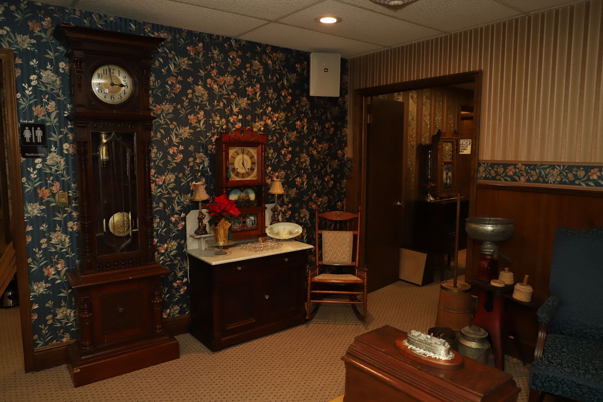Victorian-style room with floral wallpaper, grandfather clock, small sink, chair, and wooden furnishings