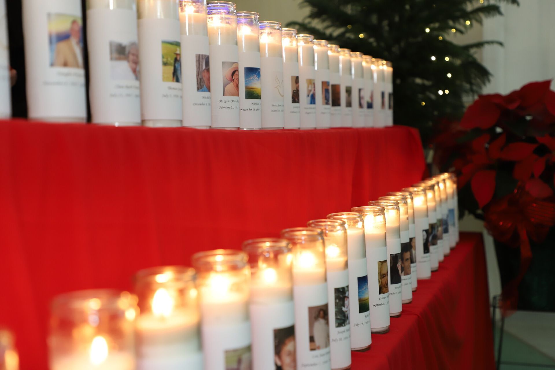 Lit candles in white glass jars lined on red draped tables, with holiday decorations in the background