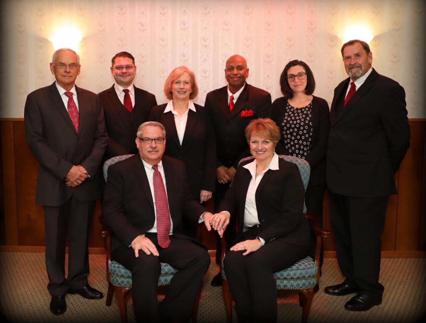 Group of seven people in business attire posing indoors for a formal group portrait.