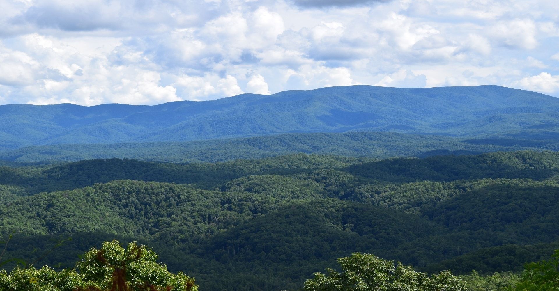 Forest-covered mountains under a cloudy blue sky, with layered ridges fading into the distance.