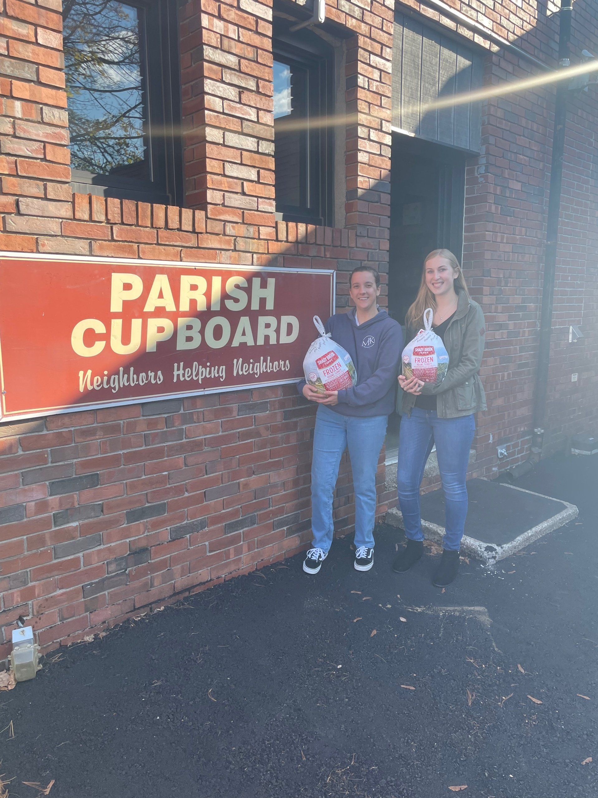 Keara Moulton and Mallory Beauregard each hold a turkey that are part of a donation in front of the entrance to The Parish Cupboard