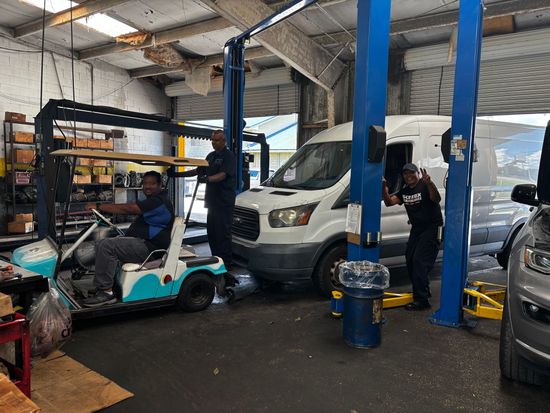 Auto repair shop with a car on a lift, a scooter in front, and mechanics working nearby