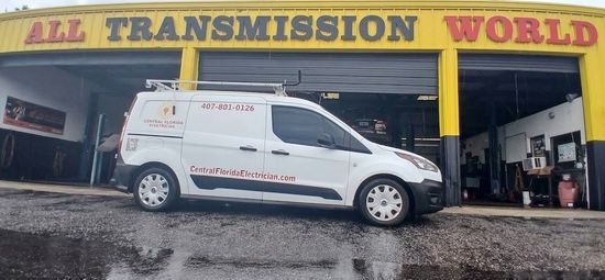 White service van parked outside All Transmission World auto shop under yellow/red signage